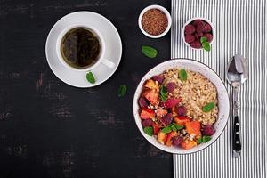 Oatmeal porridge with raspberry and peach on dark background. Healthy breakfast. Vegetarian food. Top view photo