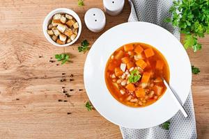 Tomato chicken soup with pumpkin and white beans in white bowl. Top view photo