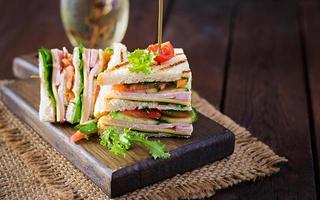 Club sandwich with ham, tomato, cucumber, cheese,  and arugula on wooden background. photo