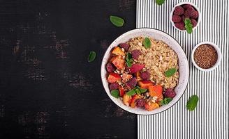 Oatmeal porridge with raspberry and peach on dark background. Healthy breakfast. Vegetarian food. Top view photo