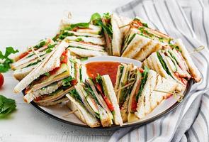 Club sandwich with ham, tomato, cucumber, cheese,  and arugula on wooden background. photo