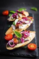 Tapas - Spanish bar food. Bruschetta with slices of sun-dried tomatoes,cheese mozzarella and anchovies on dark background. photo