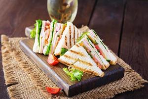 Club sandwich with ham, tomato, cucumber, cheese,  and arugula on wooden background. photo