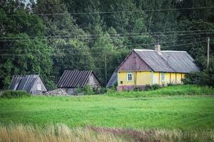 Small yellow farm house in typical surroundings of forest and grass meadow with visible field before harvest in Europe photo