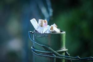 Ashtray made from the street dark green fence pole with visible fence wire with cigarette stubs inside on green blurred background photo