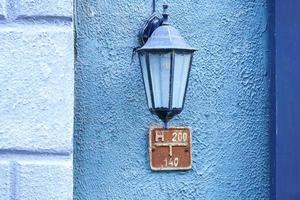 Old-fashioned street wall lamp made of black metal on blue wall facade of an old building with column and informational plaque photo