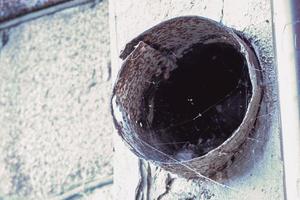 Air conditioning tube in poor condition with trash inside sticking out of concrete building wall photo