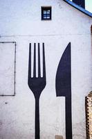 Huge fork and a knife painted in black on white building wall backside with window photo