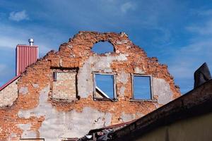 Old abandoned red brick residential building wall with windows holes without roof with visible blue sky and white clouds background photo