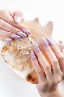 mano con largas uñas violetas cuidadas y conchas marinas foto
