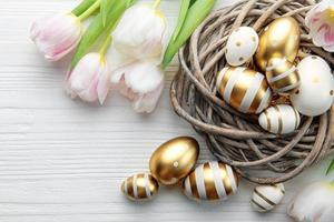 nido con Pascua de Resurrección huevos pintado dorado colores en un blanco de madera antecedentes. foto