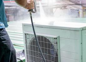 Air conditioner cleaning by a man. Technician cleans condensing unit of air conditioner by spraying water. Air conditioner maintenance service at home or office. Worker working for ac maintenance. photo