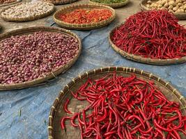 various vegetables tomatoes, chilli, red onion, corn, carrot, lime, garlic being sold at asian traditional market. colorful vegetables on round bamboo tray at traditional market floor photo