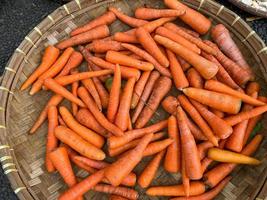 fresh, organic and imperfect carrots on round bamboo tray being sold at traditional market photo