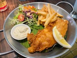 close up view of delicious fish and chips with french fries, caesar salad with balsamic sauce and tartar sauce or mayonnaise photo