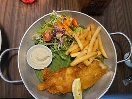 close up view of delicious fish and chips with french fries, caesar salad with balsamic sauce and tartar sauce or mayonnaise photo