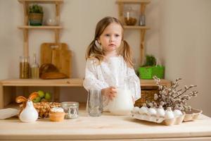 Cute little girl in a cotton dress at home in a wooden kitchen prepares an Easter cake photo