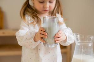 A cute little girl drinks milk at home in a wooden kitchen. Milk Day photo