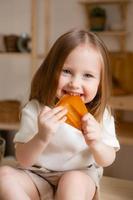 linda pequeño niña come natural pastilla a hogar en un de madera cocina. comida para niños desde natural productos foto