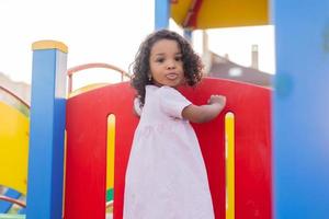 swarthy baby with curly hair in a pale pink dress plays on a street playground and rides down the hill. the concept of a healthy lifestyle. happy childhood. High quality photo