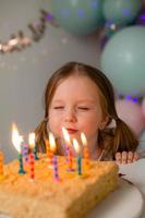 cute little girl blows out candles on a birthday cake at home against a backdrop of balloons. Child's birthday photo