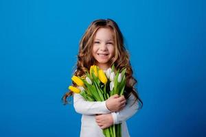 retrato de un encantador sonriente pequeño niña con un ramo de flores de tulipanes en su manos. estilo de vida. Fresco flores internacional De las mujeres día. espacio para texto. alto calidad foto