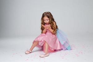 hermosa pequeño niña en un elegante rosado vestir poses sentado en un gris antecedentes y lanza papel picado. Moda y estilo. espacio para texto. foto en el estudio. alto calidad foto
