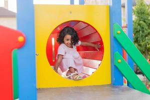 swarthy baby with curly hair in a pale pink dress plays on a street playground and rides down the hill. the concept of a healthy lifestyle. happy childhood. High quality photo