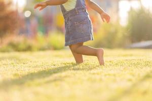 retrato pequeño contento juguetón niñito moreno niña en un mezclilla vestido de verano en pie en el jardín en un soleado día. caminando en el Fresco aire. concepto de un contento infancia. espacio para texto. alto calidad foto