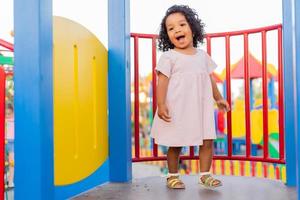 swarthy baby with curly hair in a pale pink dress plays on a street playground and rides down the hill. the concept of a healthy lifestyle. happy childhood. High quality photo