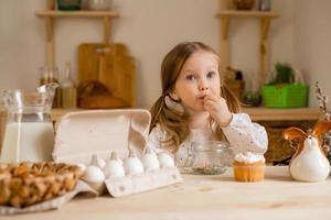 Cute little girl in a cotton dress at home in a wooden kitchen prepares an Easter cake photo