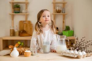 Cute little girl in a cotton dress at home in a wooden kitchen prepares an Easter cake photo