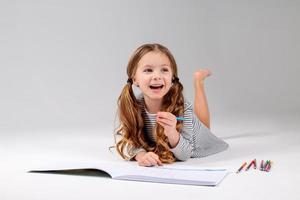 little girl in a striped dress draws in an album lying on the floor. child development. lifestyle. preschool and school education. space for text. High quality photo