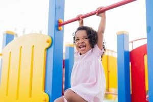 swarthy baby with curly hair in a pale pink dress plays on a street playground and rides down the hill. the concept of a healthy lifestyle. happy childhood. High quality photo