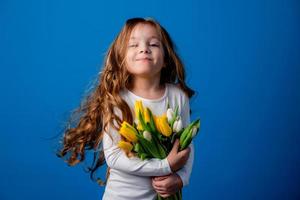 retrato de un encantador sonriente pequeño niña con un ramo de flores de tulipanes en su manos. estilo de vida. Fresco flores internacional De las mujeres día. espacio para texto. alto calidad foto