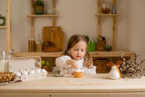 Cute little girl in a cotton dress at home in a wooden kitchen prepares an Easter cake photo