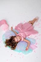 beautiful little girl in a chic pink dress lies on the floor strewn with confetti. top view. fashion and style. child celebrates his birthday. photo in the studio. space for text. High quality photo