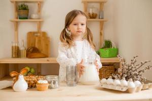 linda pequeño niña en un algodón vestir a hogar en un de madera cocina prepara un Pascua de Resurrección pastel foto