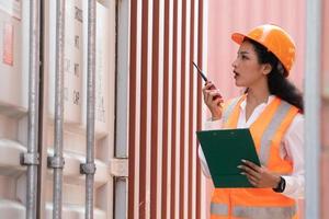 profesional asiático hembra trabajadorusando walkie-talkie en Envío yarda industrial envase caja desde carga carga Embarcacion para importar exportar. logístico, transporte. foto