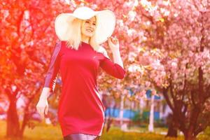 hermosa primavera niña en fragante rosado flores en verano florecer parque. mujer en un floreciente jardín . moda, productos cosméticos perfumes . Rizado rubia pelo foto