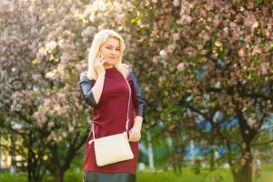 Woman with gorgeous smile having fun in blooming garden. Female with slim sexy body on natural background, wellness and fitness concept. Sensual blond girl in short chiffon dress walking in park.
