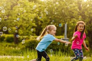 dos muchachas son contento acerca de el flotante jabón burbujas en naturaleza foto
