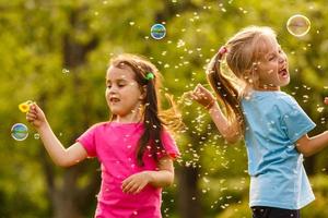 Two Little girl fun with soap bubbles in summer park, green fields, nature background, spring season photo