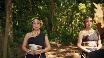 bellissimo balinese donna in esecuzione insieme con un' contento viso mentre indossare un' d'oro corona e nero vestito vicino il foresta video