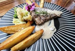 Juicy beef steak with salad and potato wedges along with pepper corn sauce photo