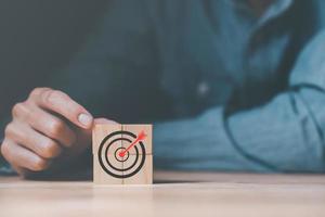 Wooden block in businessman hand and arrow icon hitting center of dartboard target,Setting business goals and focused concepts, Organizational growth and objectives, marketing strategy planning photo