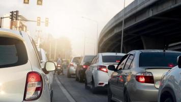 Rear side view of white car with turn on brake light. Put a traffic signal forbidden to pass in the intersection with cars parked in a queue. Blurred view of a concrete bridge under the everning sky. photo