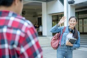 Beautiful student woman with backpack and books outdoor is greeting friends. Smile girl happy carrying a lot of book in college campus. Portrait female on international Asia University. Education photo