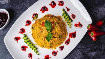 Indian biriyani rice pot served with red chili sauce and mint leave on a white plate, black background. photo