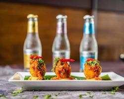 Fish kebabs with chili chutney served with red chili and coriander on a white plate with banana leaves bottles in the background. photo